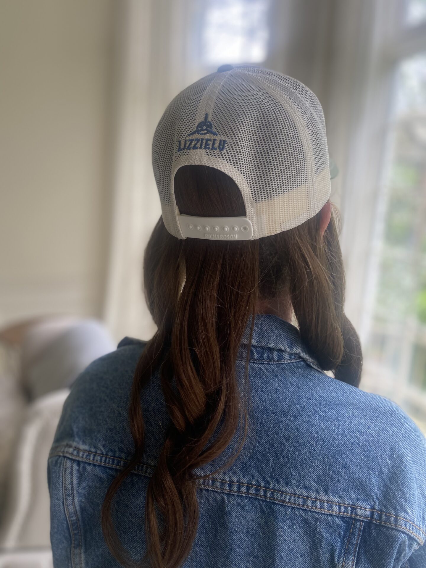 The back of a LizzieLu snapback hat with wavy brunette hair insert
